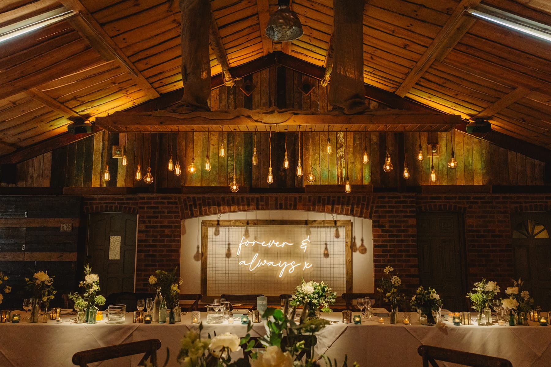 Inside Owen House Wedding Barn on a wedding evening — Edison bulbs hanging from the beams above the top table