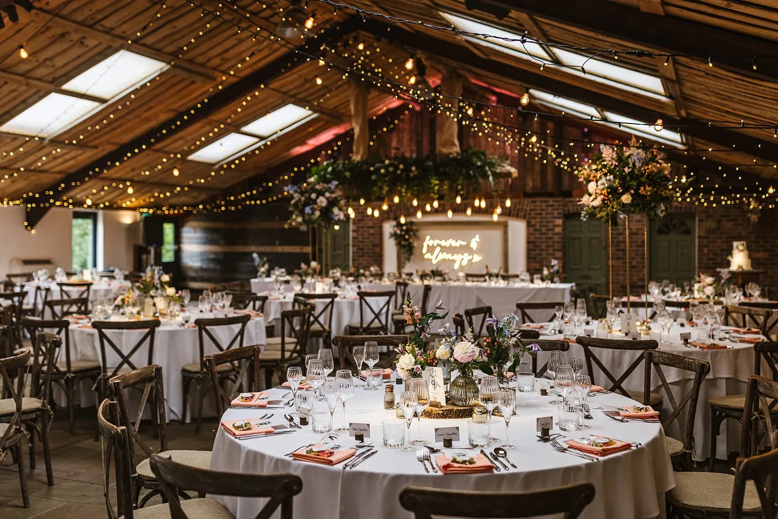 Inside Owen House Wedding Barn — strings of fairy lights under the timber roof, tables set for a wedding
